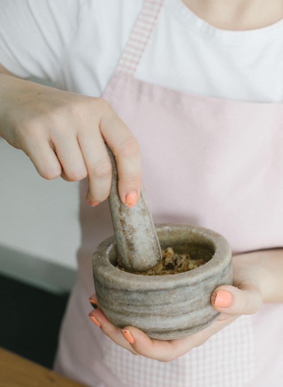 Hands grinding dried herbs with a stone mortar and pestle